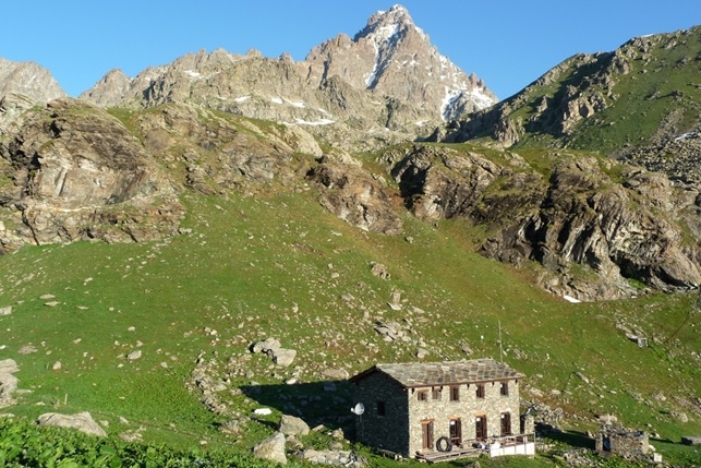 il rifugio alpetto, in pietra immerso nel verde della conca erbosa che lo ospita, sullo sfondo si ergono montagne roccioso