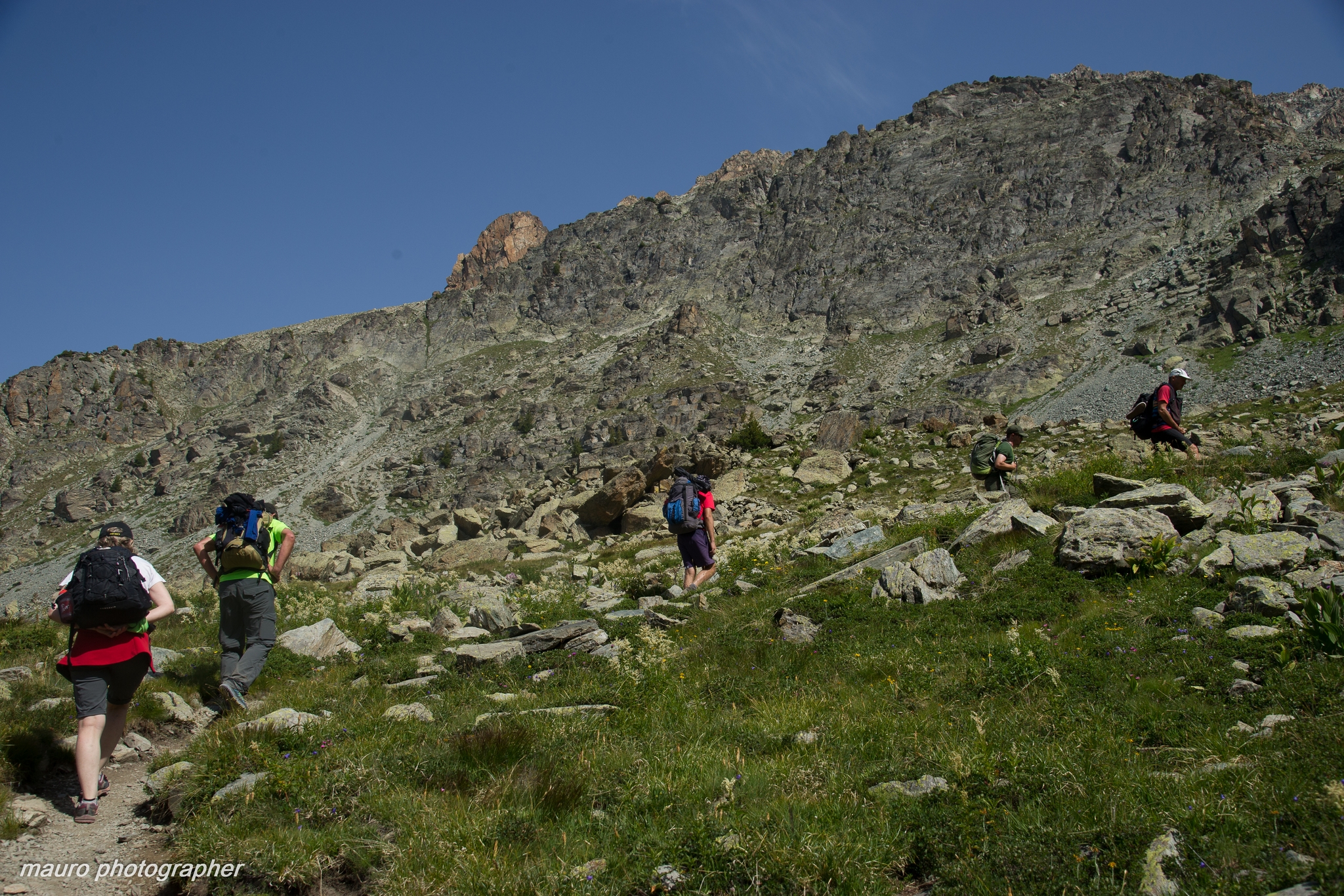 escursionisti su un sentiero tra rocce e praterie alpine, cielo azzurro