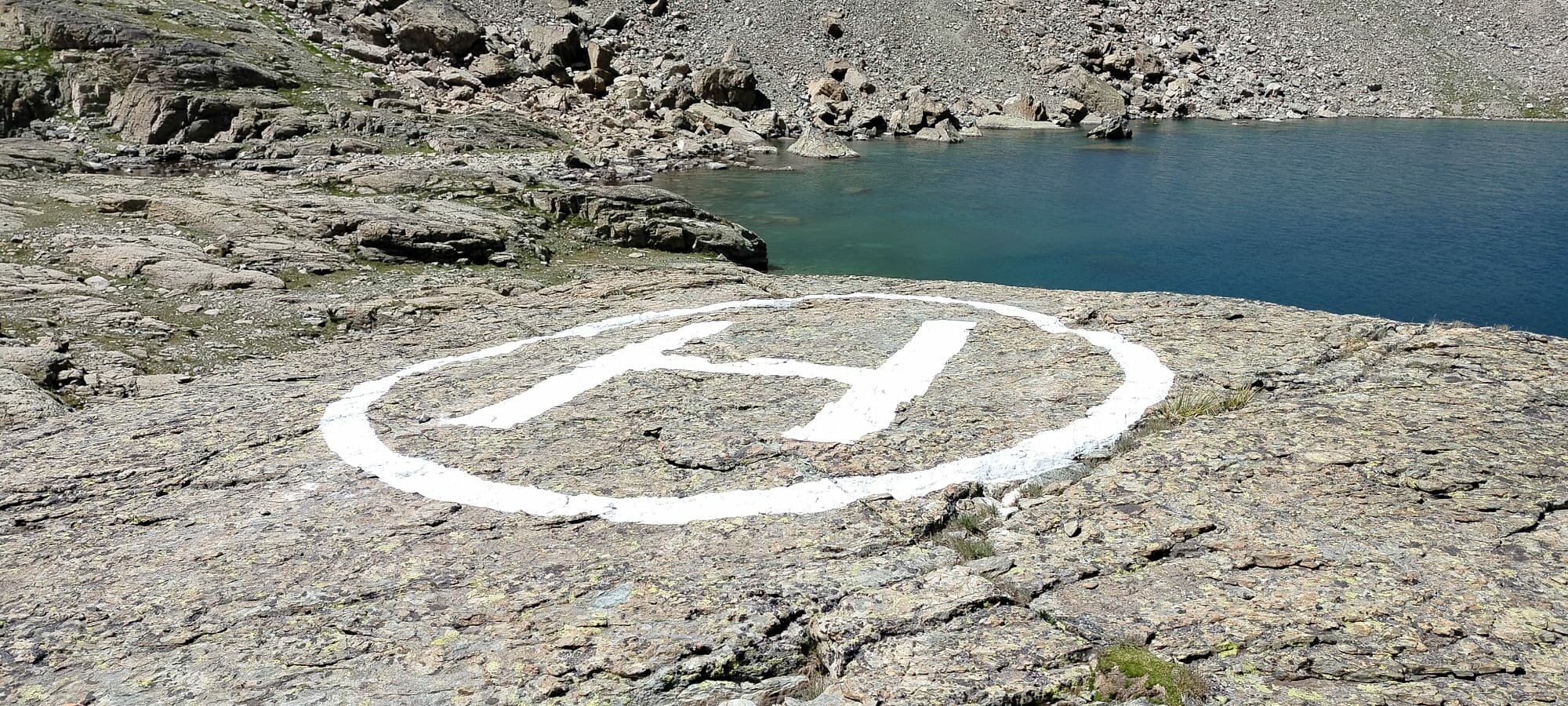 su un tratto di roccia pianeggiante e nelle vicinanze di un lago si vede una grande H in un cerchio di vernice bianca.