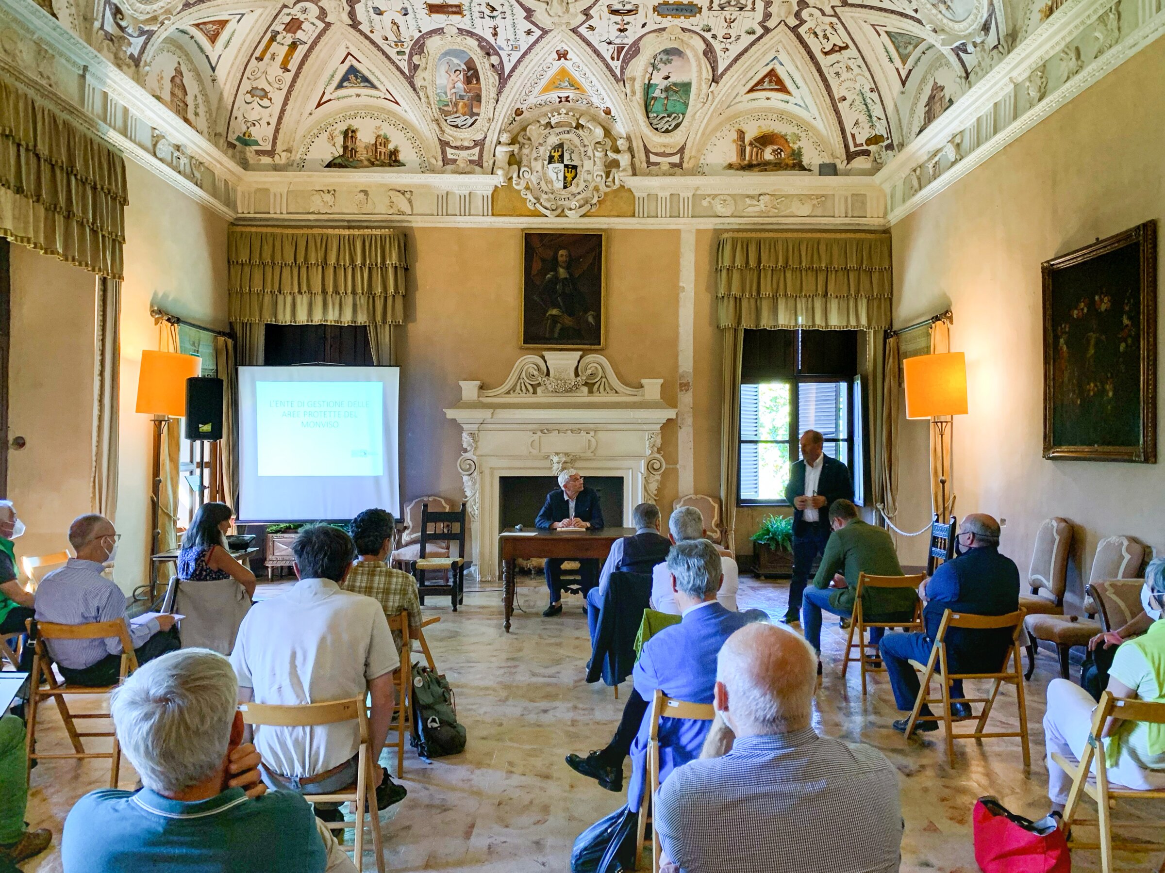 Persone sedute all'interno della Sala delle Grottesche del Castello della Manta: sta parlando il presidente del Parco del Monviso, Dario Miretti