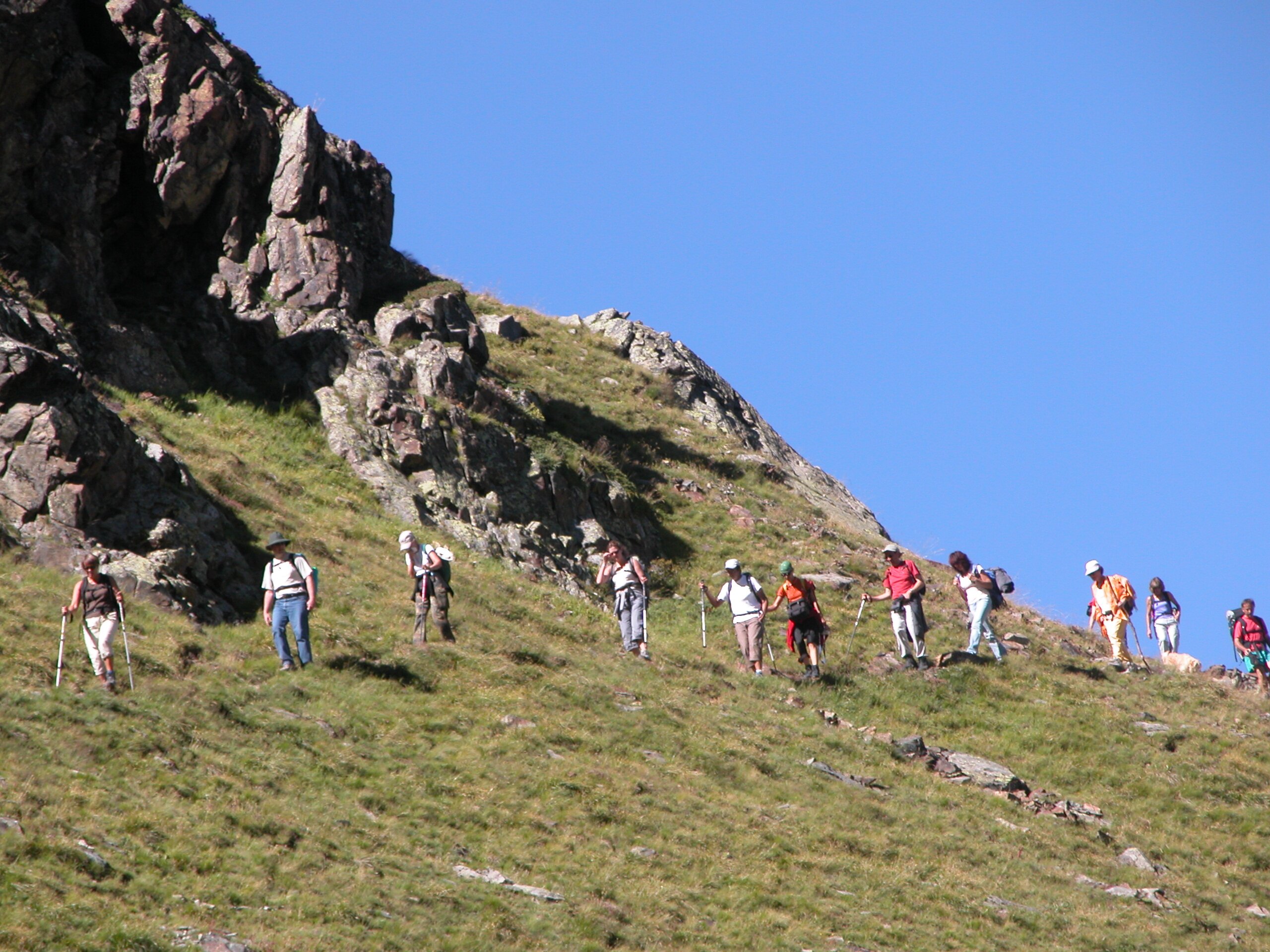 escursionisti attraversano in fila indiana il fianco di un pendio erboso. cielo azzurro