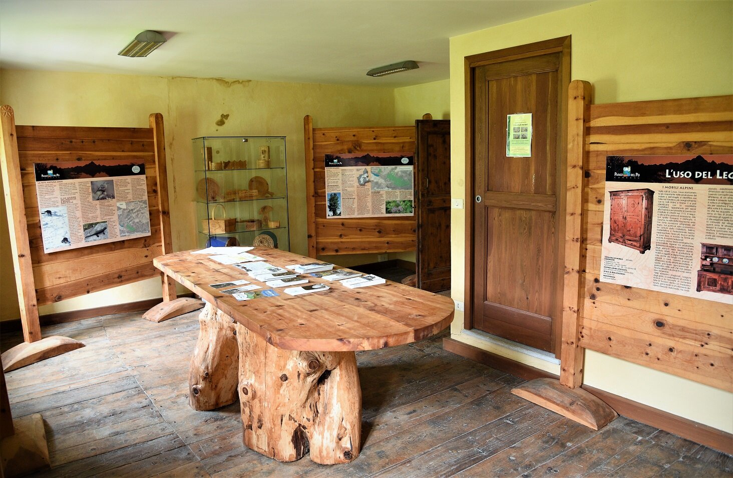 Nella foto la saletta al primo piano del Centro Visita Alevè che illustra l'utilizzo del legno di pino cembro e la storia del bosco. Sono esposti un tavolo, dei pannelli fotografici e esemplari di materiale ligneo lavorato