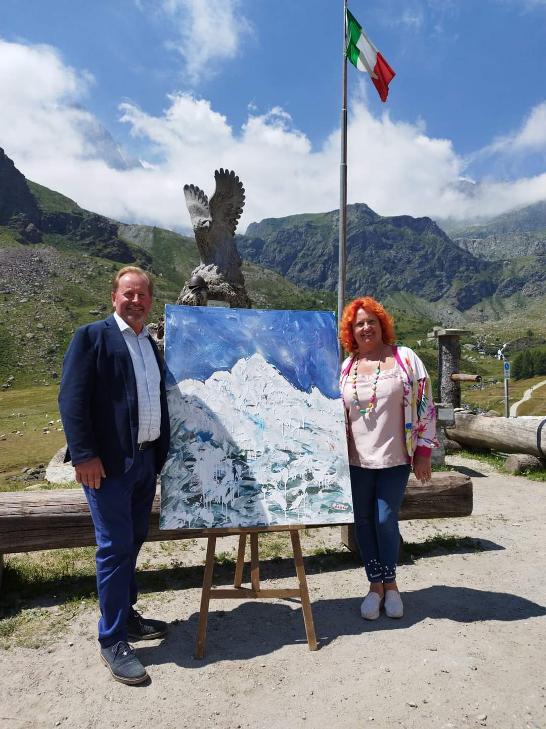 Il presidente del Parco del Monviso, Dario Miretti, con l'artista Caterina Rinaudo, in arte Katarina, in occasione dell'inaugurazione della mostra Katarina sul Monviso. Tra i due il dipinto dedicato al Monviso, sullo sfondo una bandiera italiana e i rilievi dell'alta valle Po.