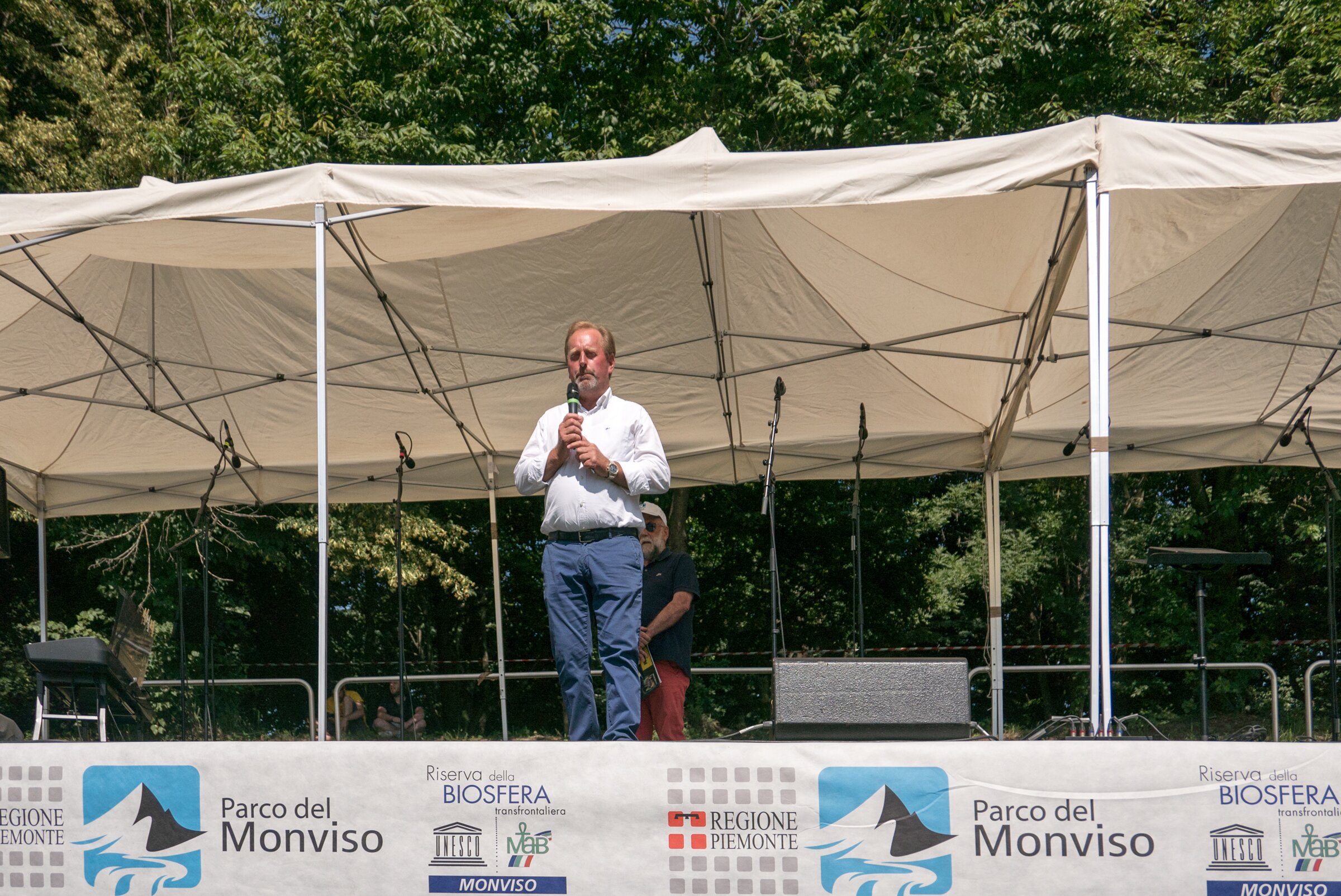 su un palco con striscioni del Parco del Monviso, il presidente Dario Miretti in camicia sta parlando ad un microfono