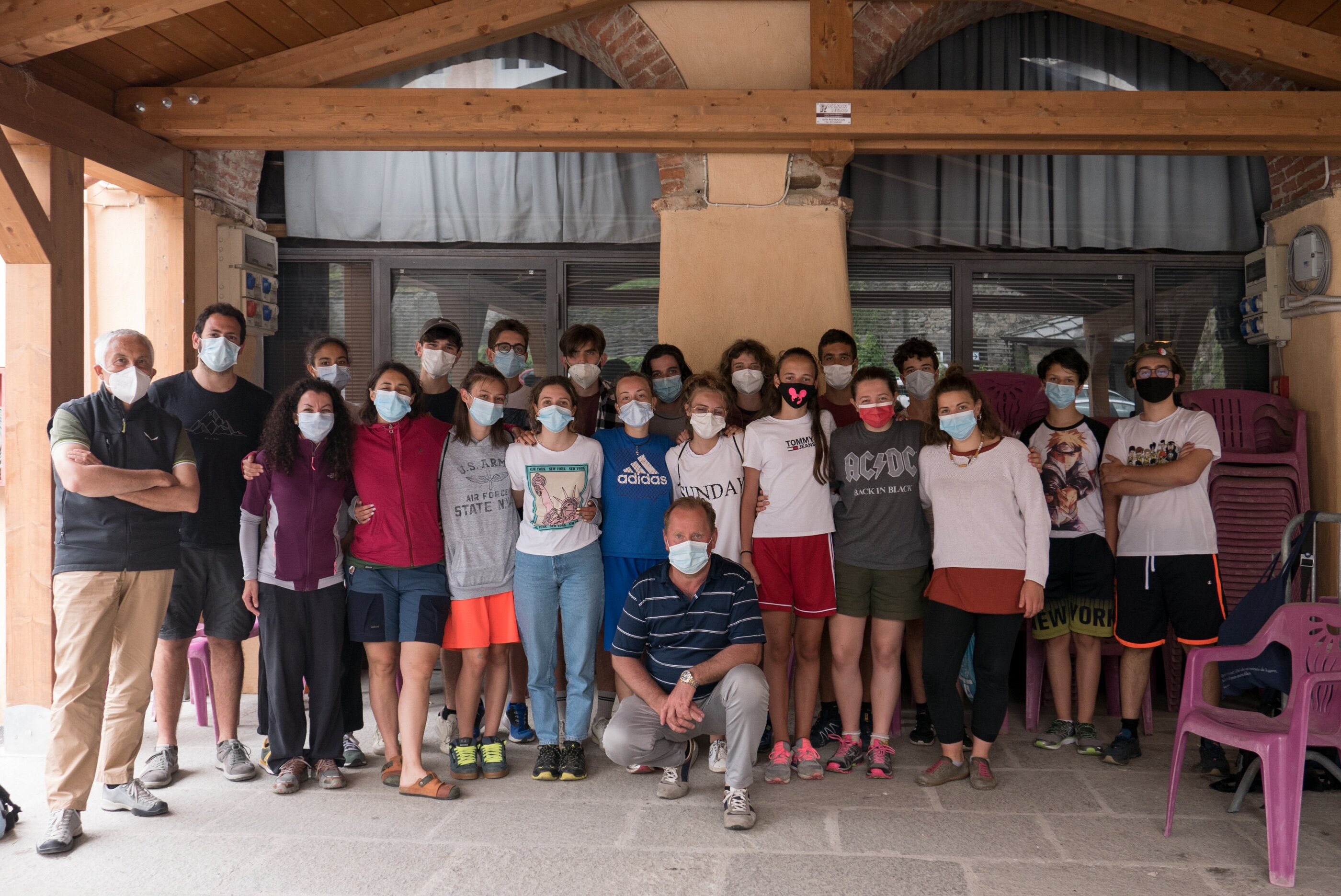 gruppo di una ventina di ragazzi, alcuni in piedi, alcuni accovacciati, con mascherina, sotto un porticato. Al centro, accovacciato, il presidente Dario Miretti