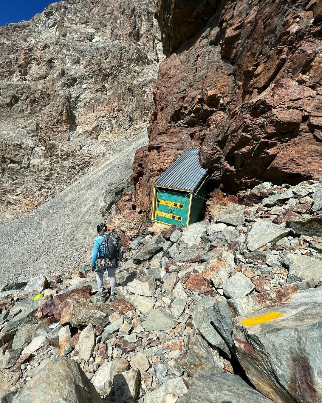 un alpinista di spalle scende verso il bivacco Andreotti, dalla parete gialla e verde; intorno, le rocce del Monviso.