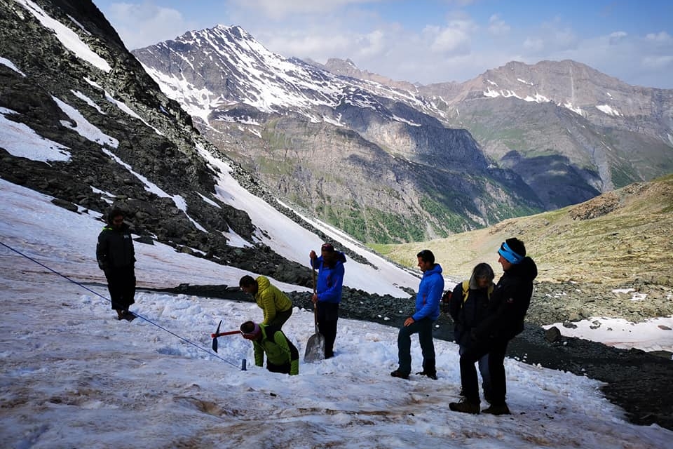 Sette persone in abiti escursionistici al lavoro nella neve per liberare l'entrata francese del Buco di Viso con picozza e pala.