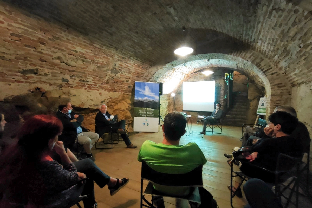 Gruppo di persone sedute in cerchio in un locale con volta a mattoni del Castello della Manta, presente un roll-up con l'immagine della Riserva della Biosfera transfrontaliera del Monviso