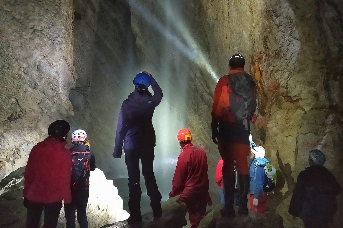 Dentro alla grotta di rio Martino (foto © Cristian Mustazzu): otto persone di spalle con abbigliamento da escursione in grotta e casco guardano la cascata che si trova al fondo della grotta di rio Martino, a Crissolo.
