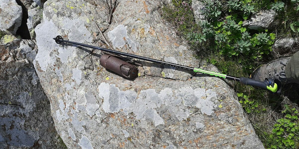 ordigno bellico della seconda guerra mondiale su una roccia, con una bacchetta da nordic walking e un piede per dare idea della dimensione dell'ordigno stesso