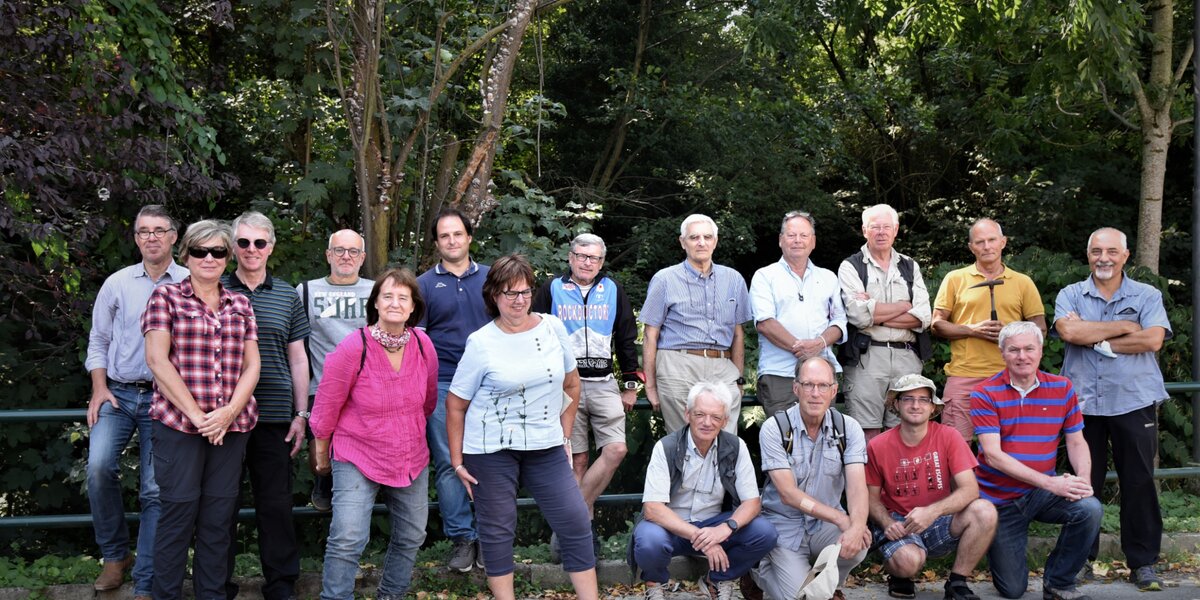 Foto di gruppo con una ventina di persone, dietro di loro piante