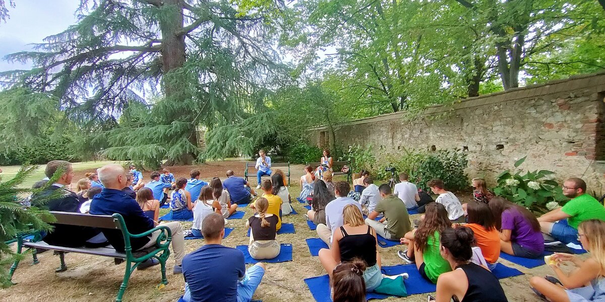 Conferenza di Fabio Fazio all'aperto, in un parco con alberi secolari: presenti molti giovani seduti su coperte sul prato