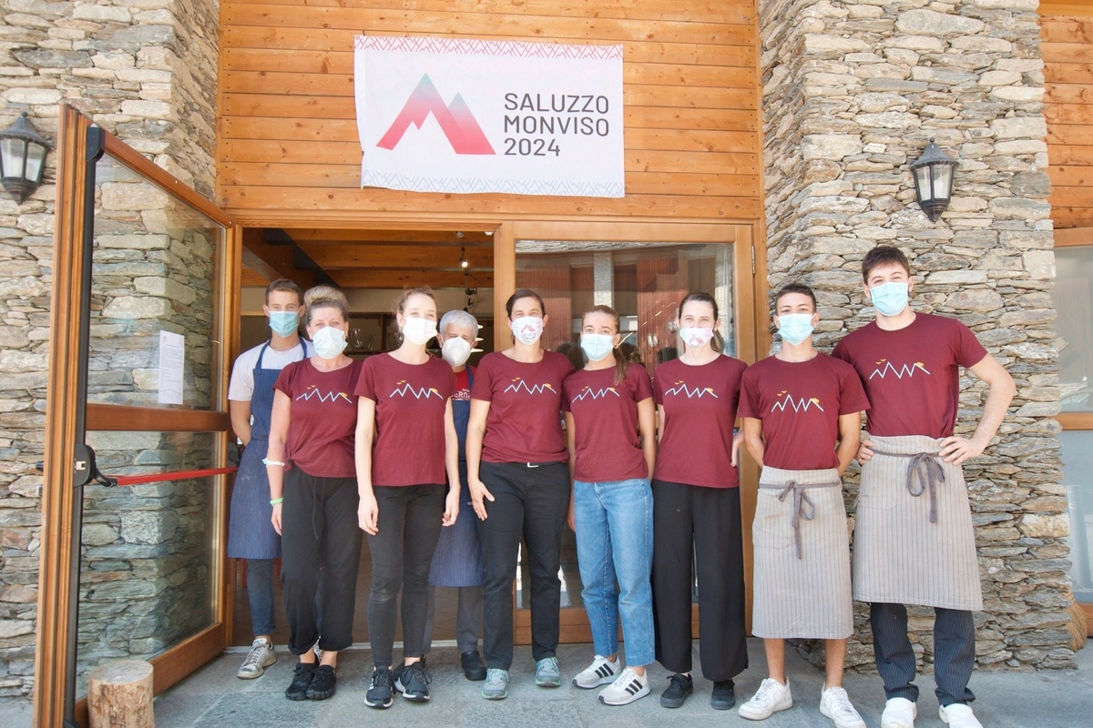 Lo staff in piedi davanti all'ingresso del rifugio, 9 persone di cui 7 con maglietta rossa e 3 con grembiule