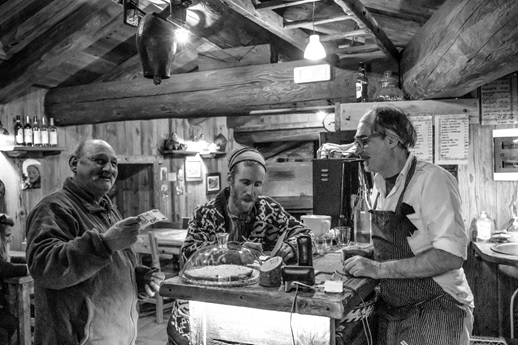 Foto in bianco e nero all'interno della locanda con due avventori e il proprietario al bancone