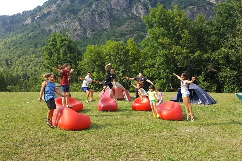 un gruppo di bambini in un prato salta tra poltrone a sacco e tende