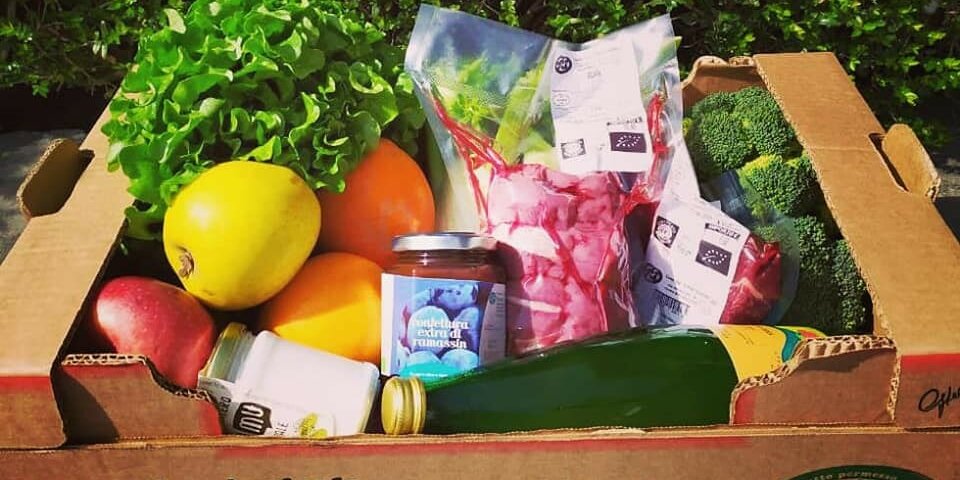 Una cassetta piena di prodotti tra cui verdura, frutta, bottiglie e vasetti
