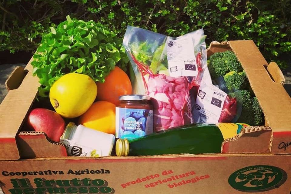 Una cassetta piena di prodotti tra cui verdura, frutta, bottiglie e vasetti