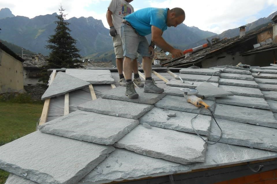 Due muratori in piedi lavorano a un tetto di lose (pietre piatte)