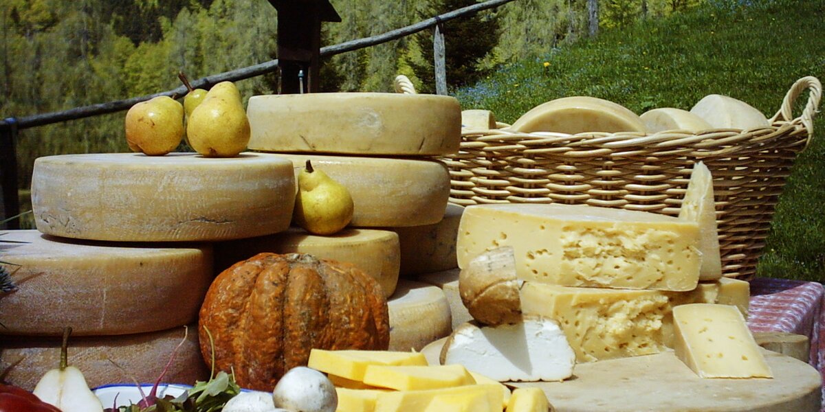 Tavola imbandita all'aperto in ambiente montano con forme di formaggio insalata, pane, zucca e pere