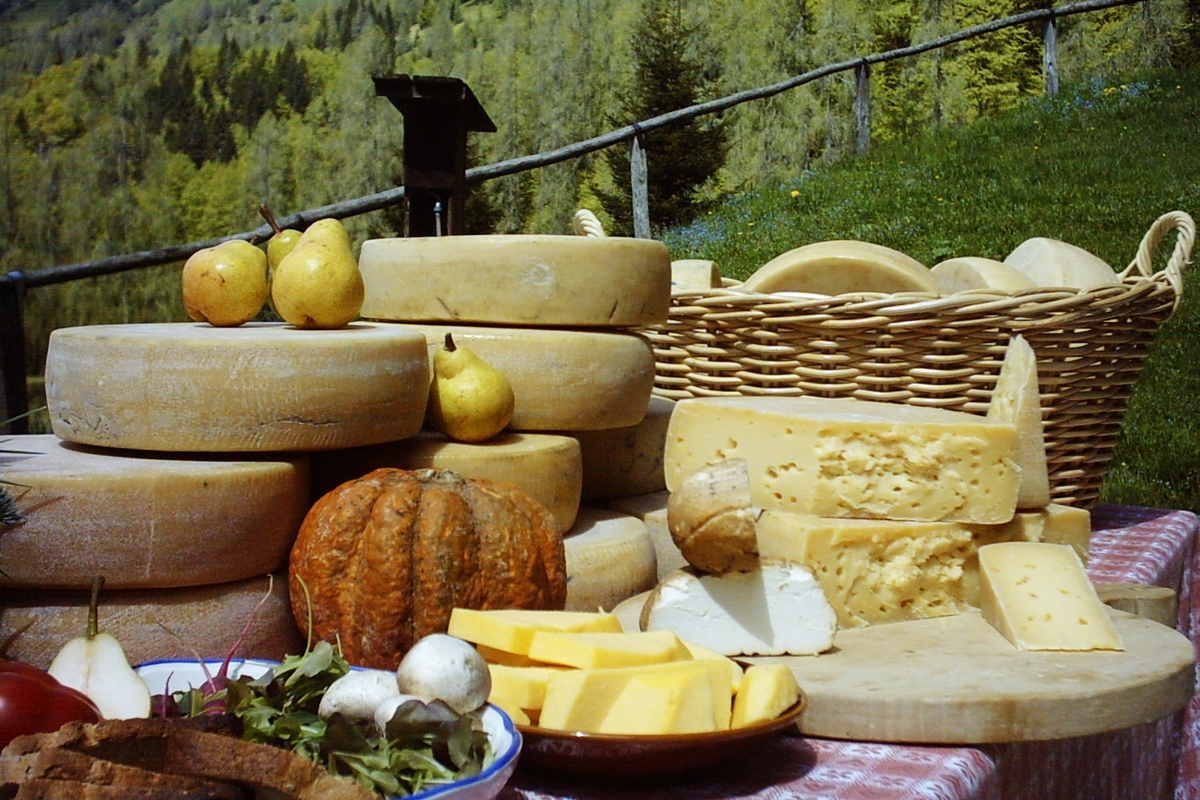 Tavola imbandita all'aperto in ambiente montano con forme di formaggio insalata, pane, zucca e pere