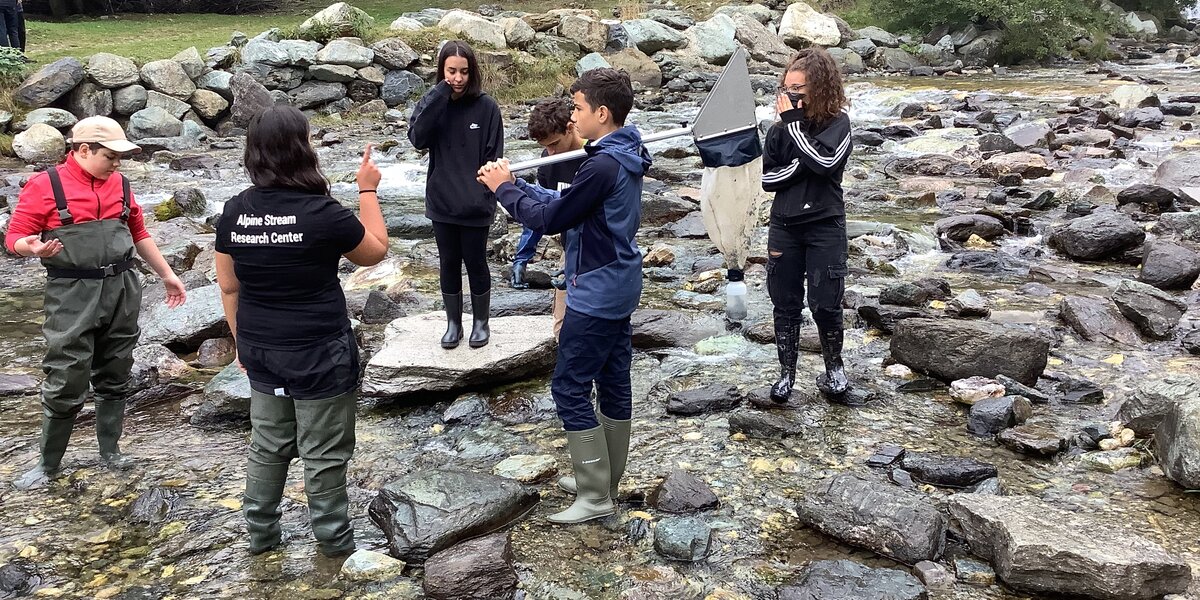 Un gruppo di studenti sul greto del fiume con cosciali; il ragazzo al centro tiene in mano un retino