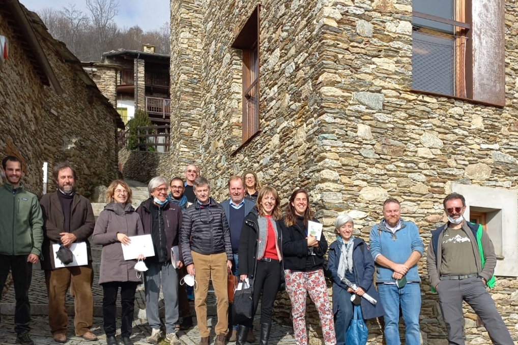 gruppo di persone davanti al centro Lou Pourtoun di Ostana, edificio in pietra a vista: quattordici tra uomini e donne
