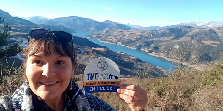 Natalia in primo piano mostra il logo della sua attività. Sullo sfondo un lago tra le montagne
