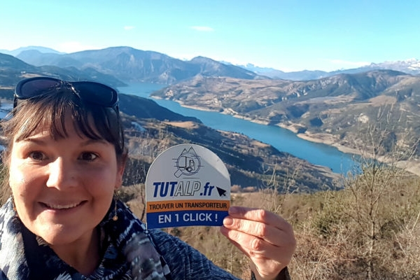 Natalia in primo piano mostra il logo della sua attività. Sullo sfondo un lago tra le montagne