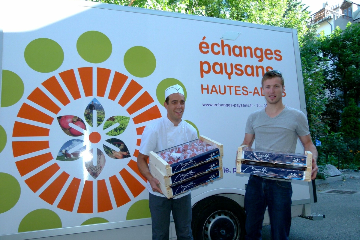 due uomini con delle cassette di frutta in mano davanti a un furgone con la scritta Echanges Paysans