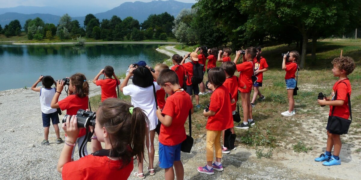 bambini con binocolo, tutti con una maglietta rossa, guardano verso le anse di un fiume a poca distanza da loro