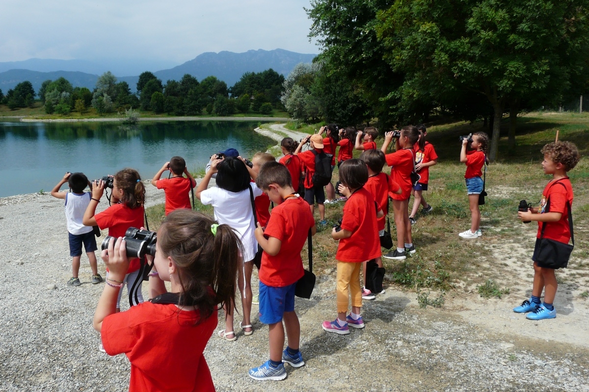 bambini con binocolo, tutti con una maglietta rossa, guardano verso le anse di un fiume a poca distanza da loro