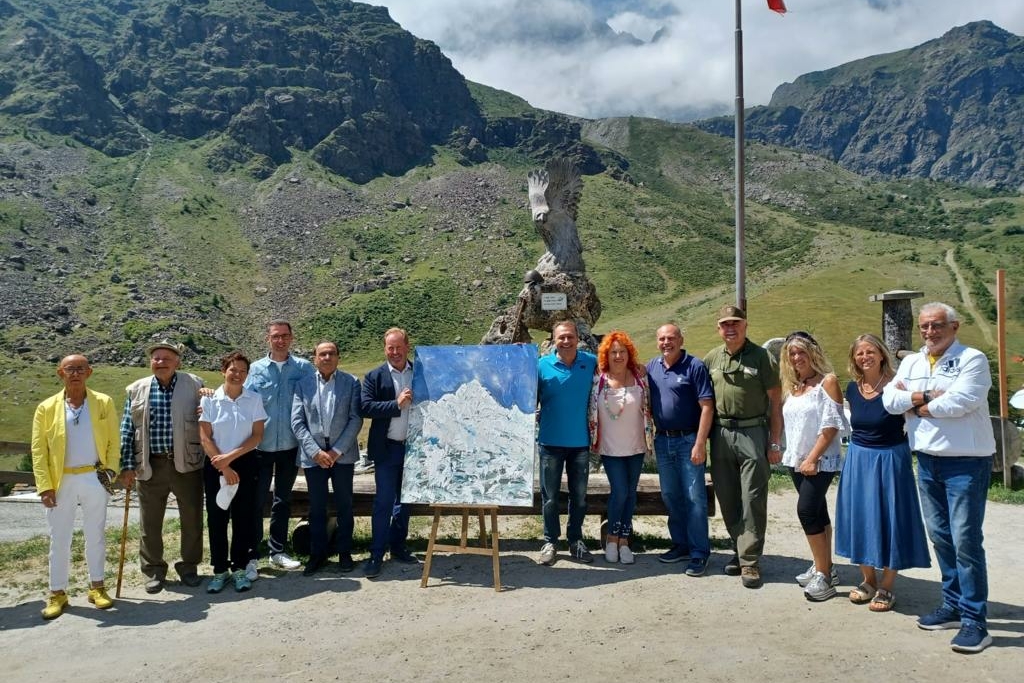 Un gruppo di persone ai due lati di un dipinto che raffigura il Monviso; sullo sfondo i rilievi dell'alta valle Po con un cielo coperto da nuvole