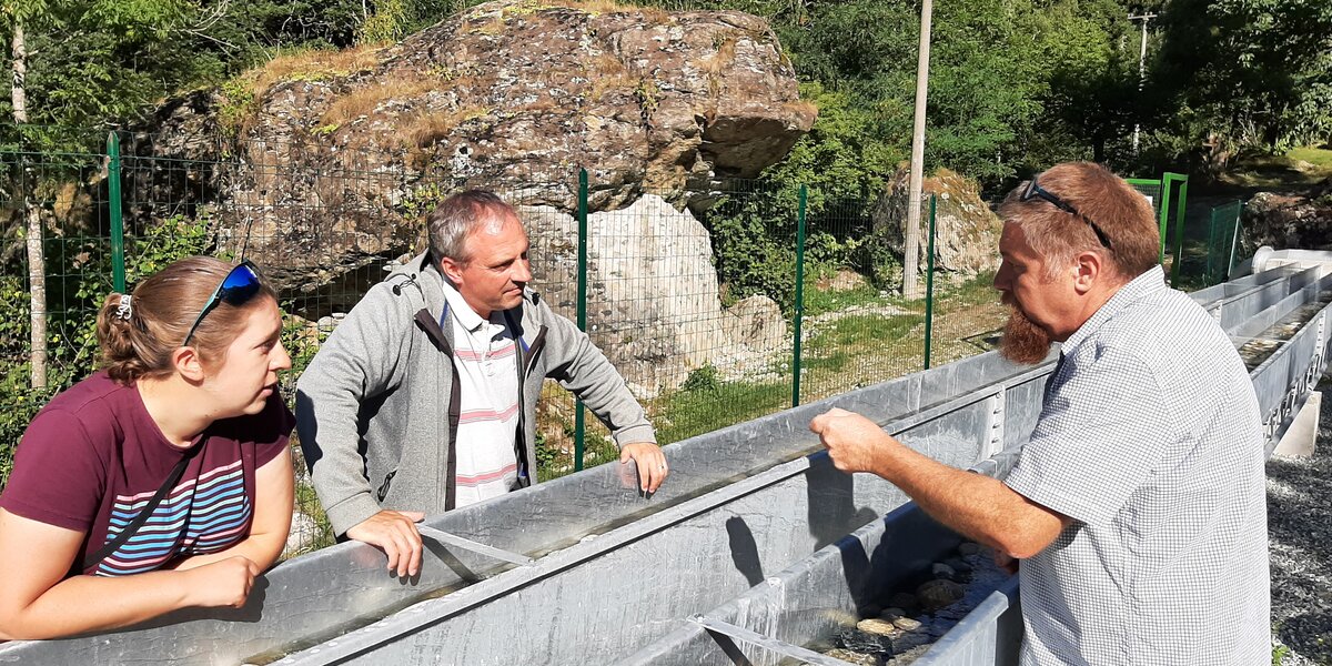 in un ambiente boscato, in primo piano vi sono tre persone ai lati di un paio di grosse canaline in metallo, nelle quali scorre l'acqua e sul cui fondo si trovano pietre fluviali: le canaline sono artificiali e sono state costruite per simulare gli ambienti fluviali a scopo di studio.