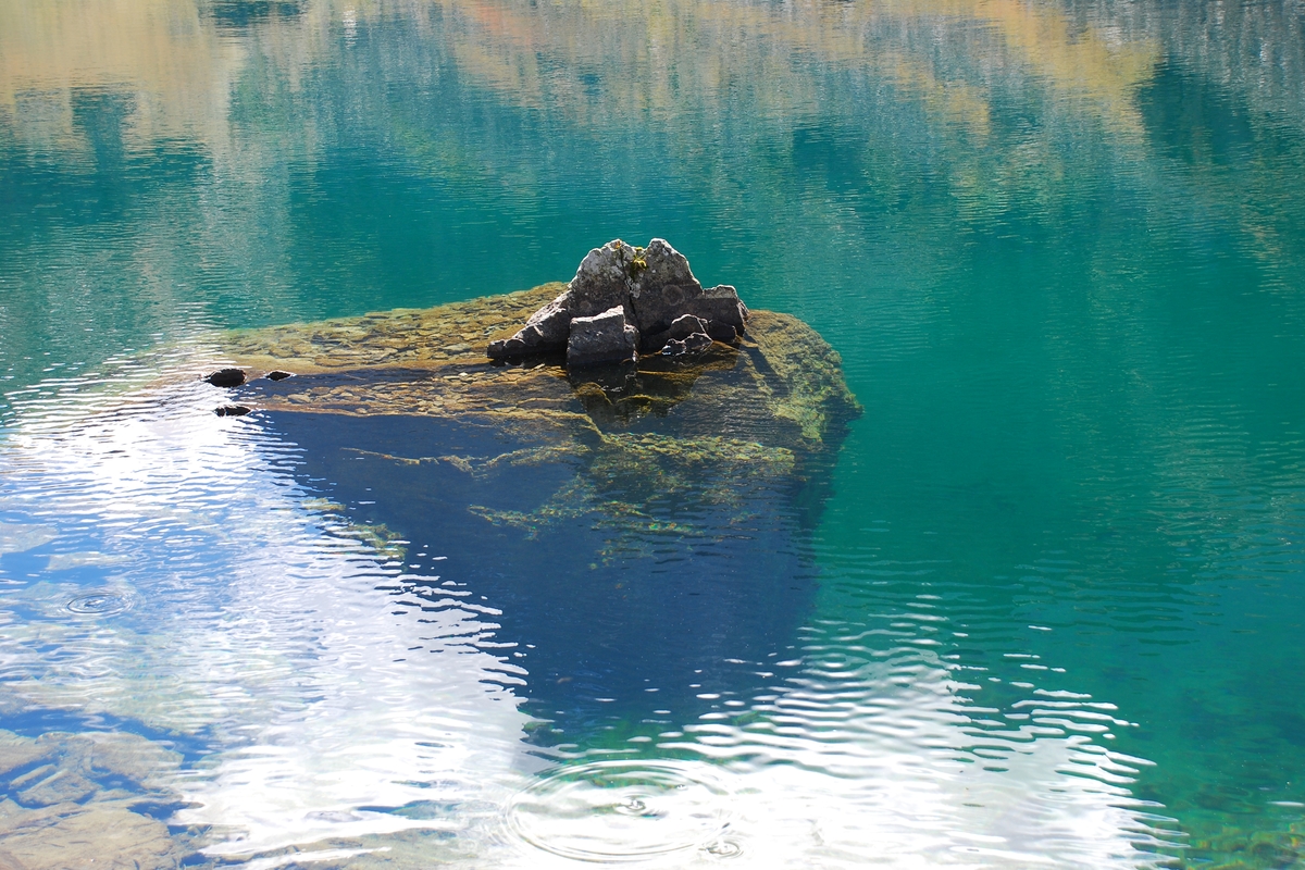 Un sasso emerge dalle acque del lago che riflettono i colori circostanti