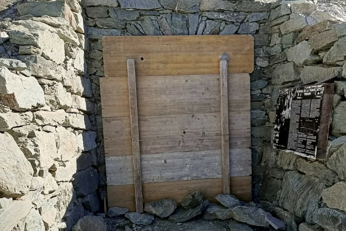 Assi di legno poste a chiudere il lato francese di Buco di viso; dietro le assi si vede l'architrave con arco in pietra. sulla destra si intravede il cartello informativo dedicato al traforo