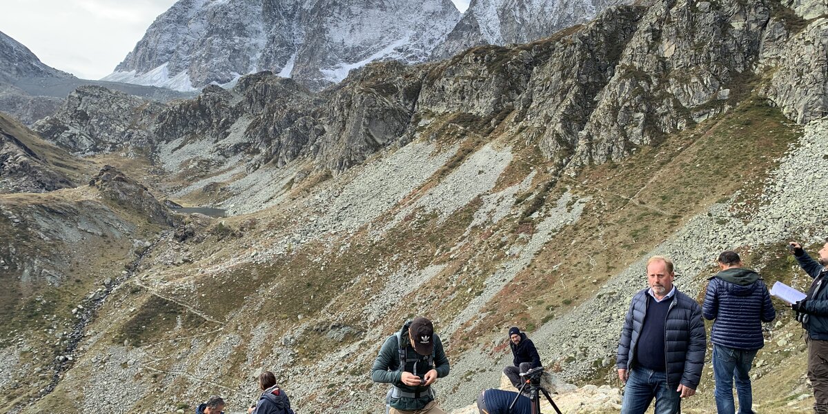 una troupe televisiva si prepara a registrare al Pian del Re, Crissolo. In primo piano c'è anche il presidente del Parco del Monviso, Dario Miretti. Sullo sfondo il Monviso.