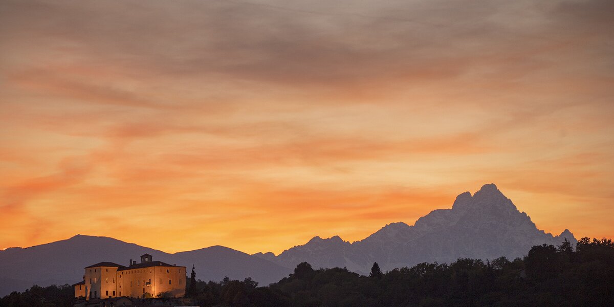 panorama al tramonto nel quale si vede in basso a sinistra il Castello di Manta, tenuamente illuminato dai lampioni del suo parco, e a destra il Monviso.
