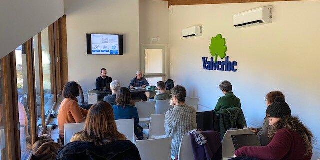 gruppo di persone sedute di spalle, con due relatori seduti ad un tavolo di fronte. sulla parete destra si legge il nome dell'azienda che ospita l'incontro, Valverbe di Melle.