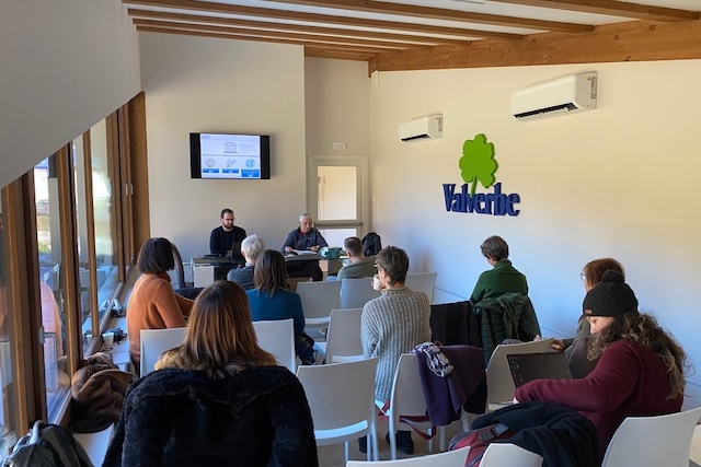 gruppo di persone sedute di spalle, con due relatori seduti ad un tavolo di fronte. sulla parete destra si legge il nome dell'azienda che ospita l'incontro, Valverbe di Melle.