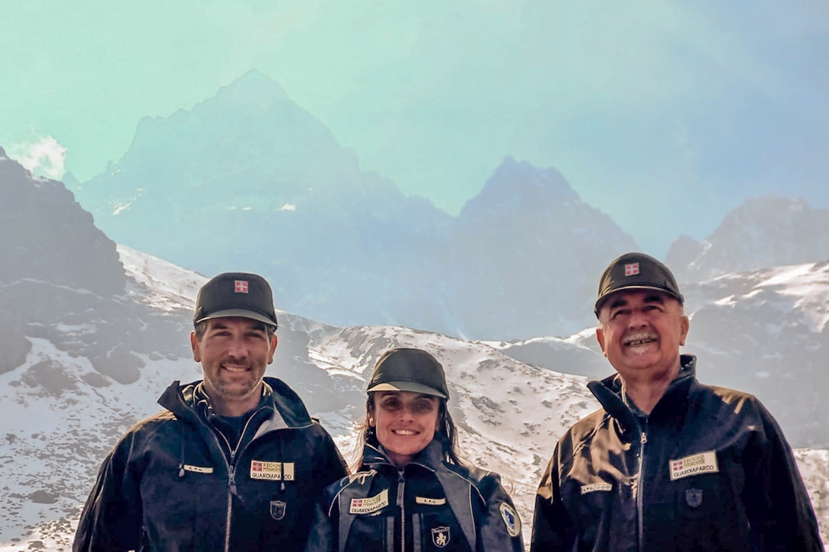 Tre persone in primo piano, a mezzo busto, davanti ad uno sfondo nel quale spicca il Monviso