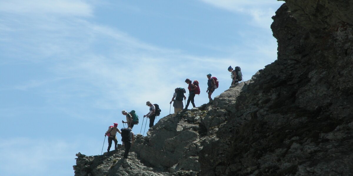 Escursionisti verso il Colle delle Traversette: immagine scattata dal basso verso l'alto in cui si vede la silhouette di alcune persone che risalgono il versante, con il cielo dietro