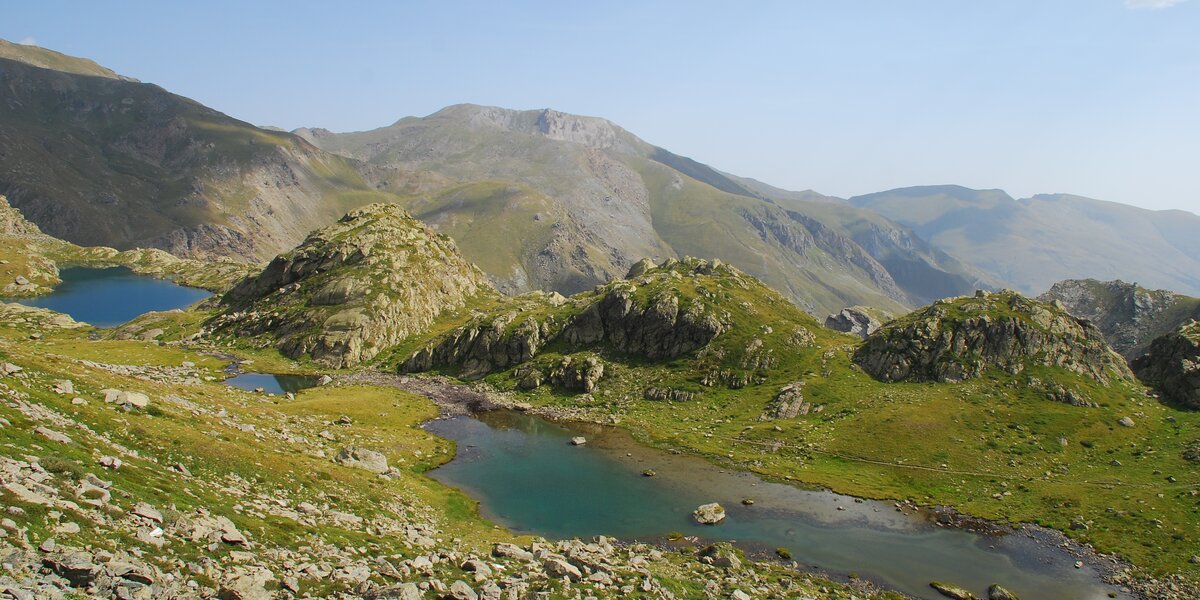 Due laghi alpini su un pianoro erboso tra le montagne, cielo azzurro
