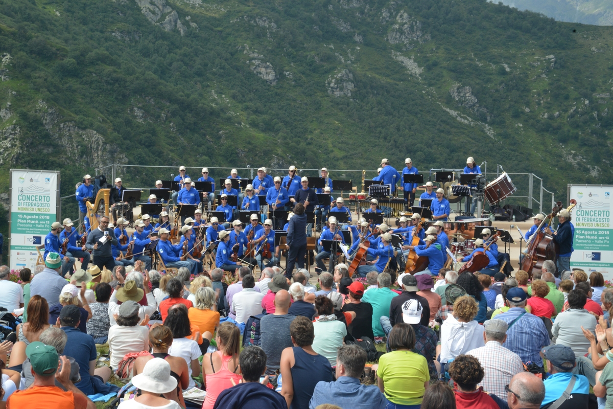 foto di repertorio della scorsa edizione del Concerto di Ferragosto a Paesana, del 2018: nella parte bassa dell'immmagine il pubblico di schiena, seduto per terra, in alto l'orchestra intenta a suonare.