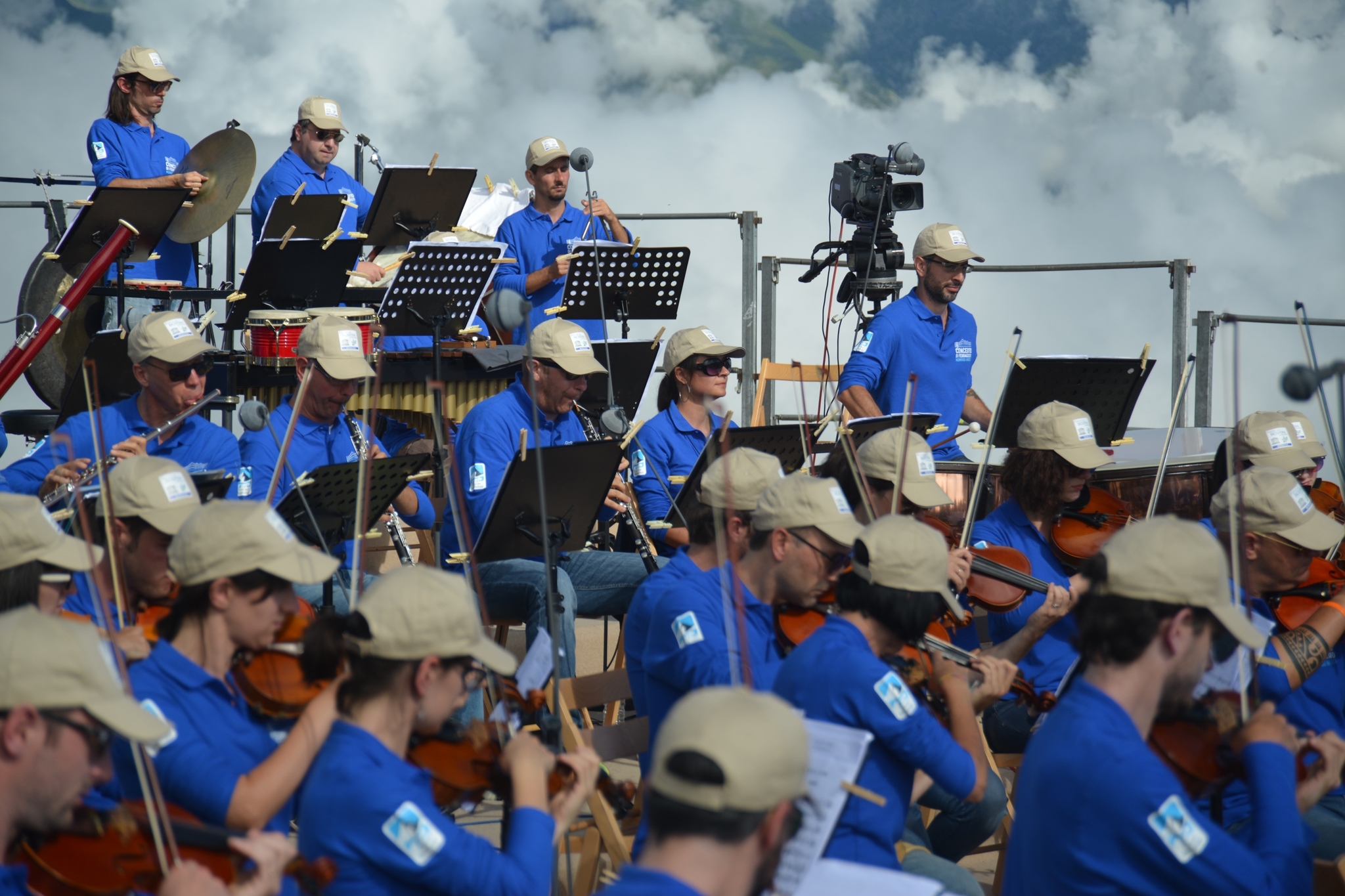 elementi di un'orchestra suonano in un contesto all'aperto: nuvole dietro al palco, in alto a destra nella fotografia