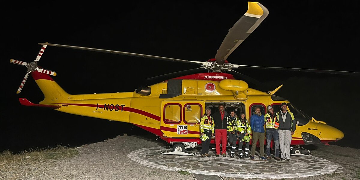 un elicottero fermo sull'elisuperficie del rifugio, nella notte del collaudo. Davanti al velivolo alcune persone.