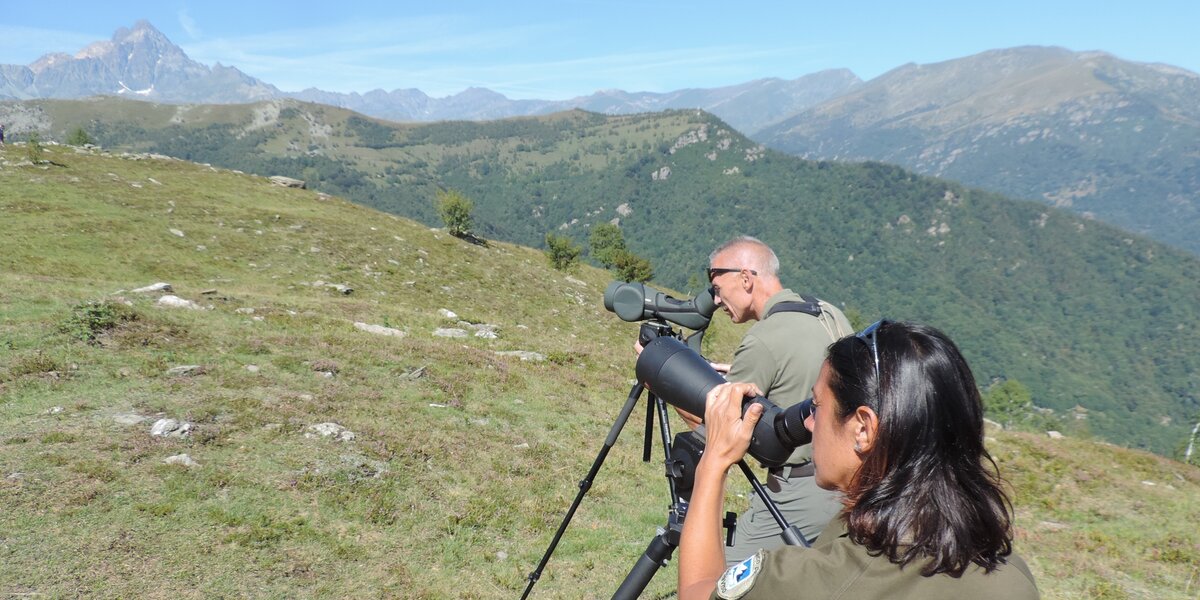 due persone, in basso a destra nella foto e colte a bezzo busto, sono intente ad osservare il cielo con dei binocoli. Sullo sfondo, si vede il Monviso.