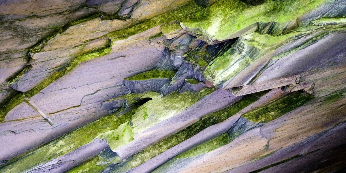 immagine ravvicinata della cava di ardesia: si vede la pietra scura con i caratteristici tagli quasi regolari e qualche riflesso verde in alto a destra.