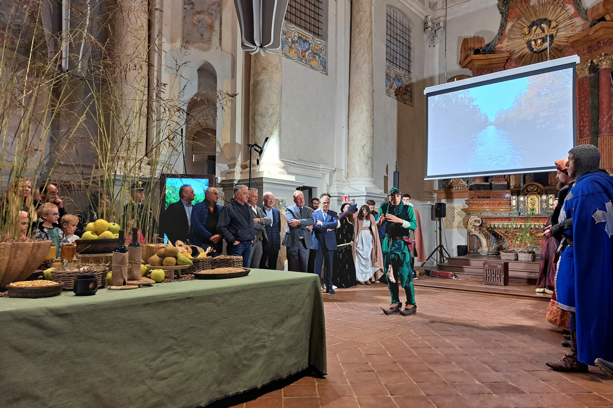 all'interno della ex chiesa del Monastero della Stella, sul lato sinostro della foto si vede uno dei tavoli dell'allestimento, con prodotti gastronomici. Dietro e a fianco, il pubblico che ascolta lo spettacolo del giullare Nespolo, visibile al centro della fotografia.