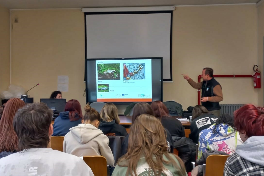 un funzionario del Parco del Monviso di fianco a una lavagna luminosa sta spiegando ad una classe di studenti, che si vede di spalle, l'etologia della Salamandra di Lanza.