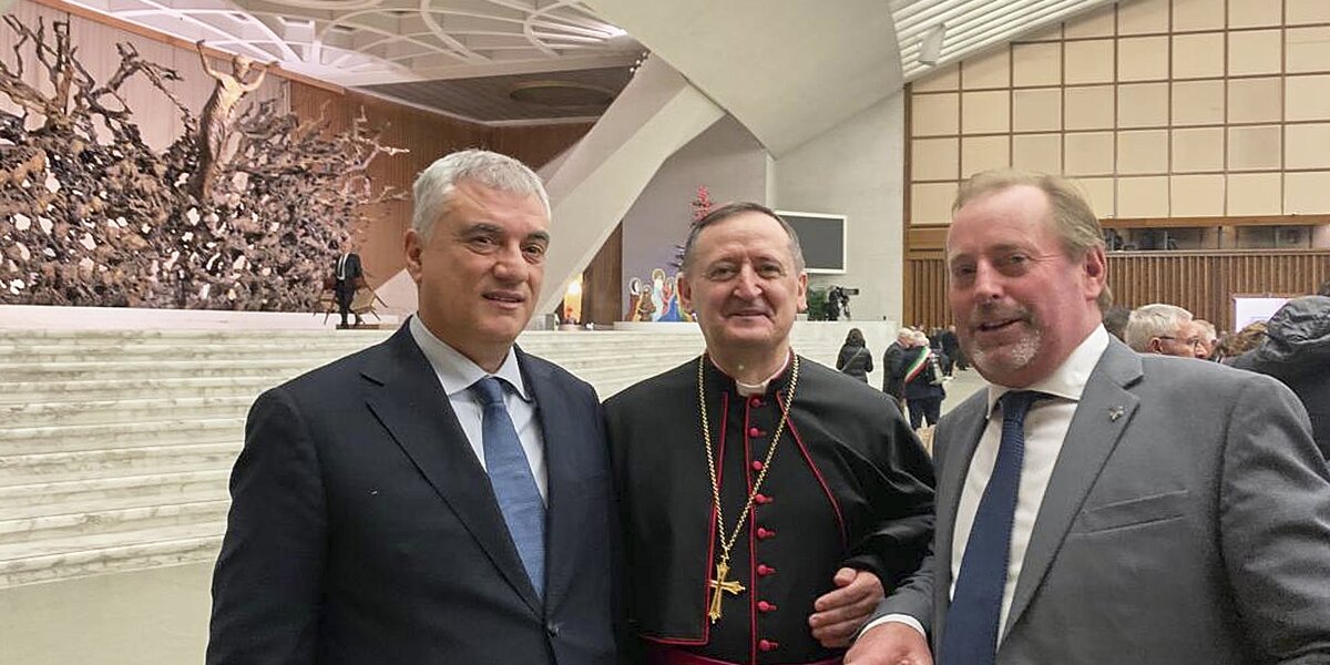 Tre persone in primo piano: al centro c'è il vescovo di Saluzzo e ai suoi lati i due presidenti delle Riserve MaB Unesco del Monte Peglia, a sinistra, e del Monviso, a destra. Sullo sfondo si riconosce la sala Paolo VI in Vaticano.